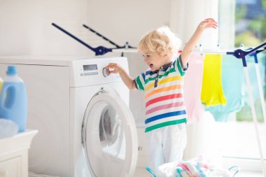 Çocuk Çamaşırhane, çamaşır makinesi ile Oda veya kurutma. Çocuk ile aile işleri yardımcı. Modern ev aygıtları ve çamaşır deterjan beyaz güneşli evinde. Raf kurutma üzerinde temiz yıkanmış kıyafetler. 