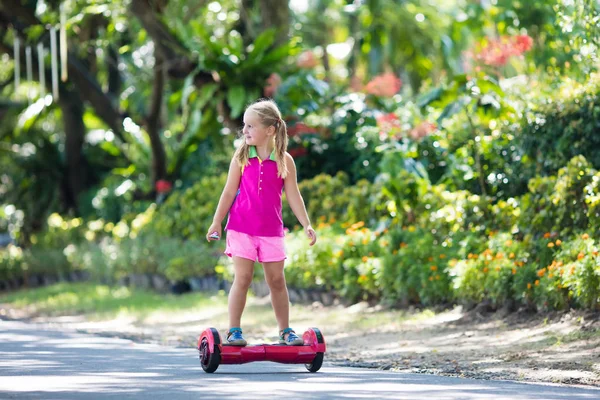 ホバー基板上の子 夏の公園でスクーターに乗る子供 子供のためのバランス ボード 電気釣り合っている都市通りのスクーター ホバーボードを乗ることを学習の女の子 学校の子供のための現代的なガジェット — ストック写真