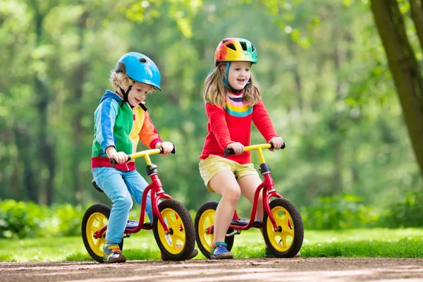 子供たちは バランスの自転車に乗って 日当たりの良い公園で自転車に子供 小さな女の子と男の子の暖かい夏の日にグライダー自転車に乗る バランスをとることを学ぶ幼児は 安全なヘルメットで自転車を実行します 子供のためのスポーツ — ストック写真
