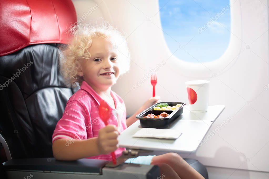 Child in airplane window seat. Kids flight meal. Children fly. Special inflight menu, food and drink for baby and kid. Little boy eating healthy lunch in airplane. Travel with kids. Family vacation.  
