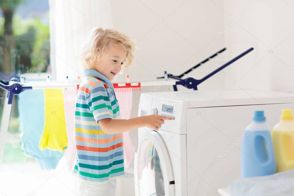 Child in laundry room with washing machine or tumble dryer. Kid helping with family chores. Modern household devices and washing detergent in white sunny home. Clean washed clothes on drying rack. 