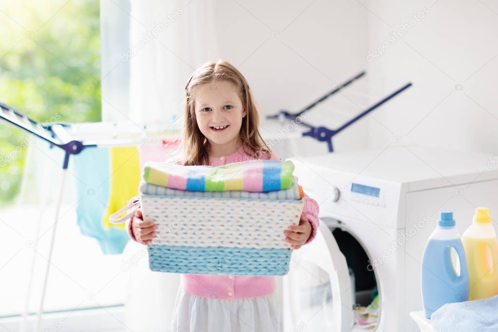 Child in laundry room with washing machine or tumble dryer. Kid helping with family chores. Modern household devices and washing detergent in white sunny home. Clean washed clothes on drying rack. 