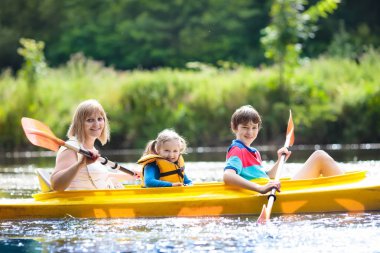 Kano üzerinde kürek çeken çocuk. Çocuklar için yaz kampı. Ailemle kano ve kano gezisi. Kanodaki çocuklar. Aile kano gezisinde. Yaz tatilinde vahşi doğa ve su eğlencesi. Kamp ve balıkçılık.
