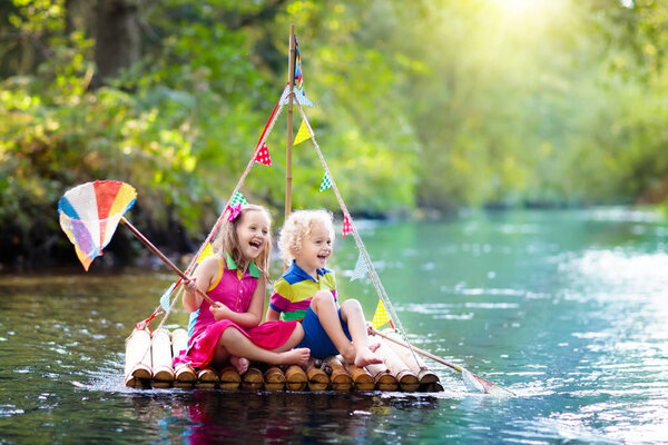 Two children on wooden raft catching fish with a colorful net in a river and playing with water on hot summer day. Outdoor fun and adventure for kids. Boy and girl in toy boat. Sailor role game.
