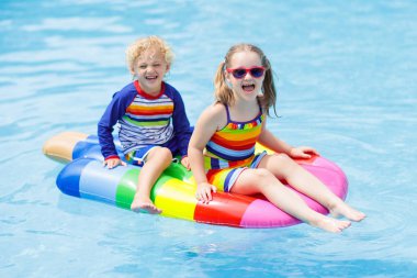 Erkek ve kız üzerinde şişme buz krem tropikal tatil köyü Açık Yüzme havuzunda yüzer. Çocuklarla yaz tatili. AIDS yüzmek ve çocuklar için giyim. Su oyuncakları. Renkli salda yüzen küçük çocuk.