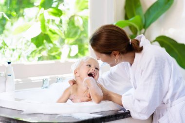 Köpük banyosu ile büyük Bahçe Manzaralı pencere güzel banyo alarak küçük bir çocuk. Anne bebek yıkama. Çocuklar hijyen. Şampuan, saç tedavisi, sabun çocuklar için köpük. Anne banyo çocuk büyük küvette. 