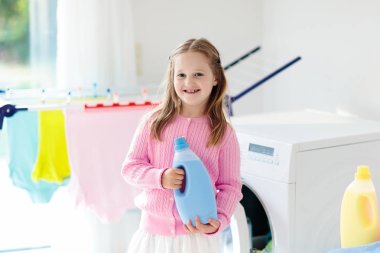 Çocuk Çamaşırhane, çamaşır makinesi ile Oda veya kurutma. Çocuk ile aile işleri yardımcı. Modern ev aygıtları ve çamaşır deterjan beyaz güneşli evinde. Raf kurutma üzerinde temiz yıkanmış kıyafetler. 