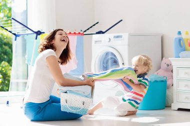 Anne ve çocuklar Çamaşırhane, çamaşır makinesi ile Oda veya kurutma. Aile işleri. Modern ev aygıtları ve çamaşır deterjan beyaz güneşli evinde. Raf kurutma üzerinde temiz yıkanmış kıyafetler. 