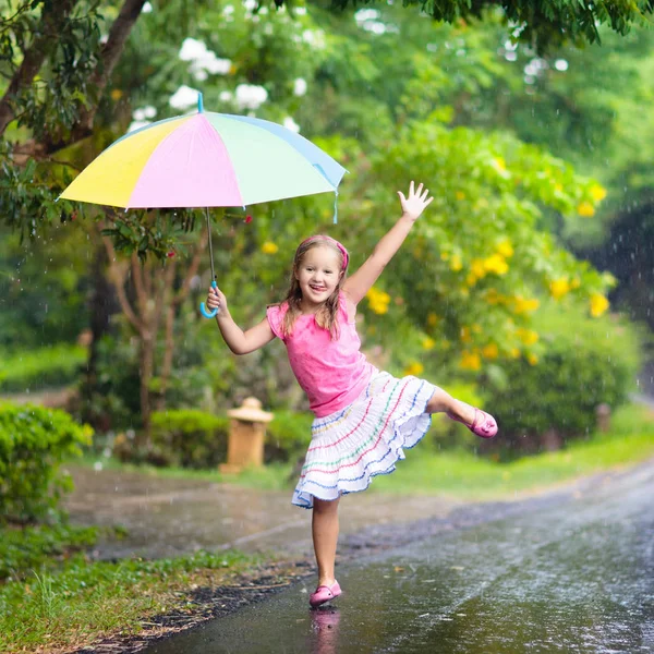 雨の中で遊んでいる子供 大雨の中 傘を差した子供たちが屋外で遊ぶ 少女は最初の春のシャワーに巻き込まれた 雨の秋の天気で子供たちの屋外の楽しみ 熱帯低気圧の中を走る子供 — ストック写真