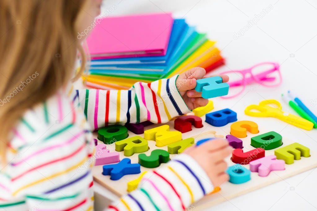 Child doing homework for school at white desk. Wooden educational abc toy puzzle for kids. Happy back to school student. Kid learning alphabet letters. Little girl with school supplies and books.