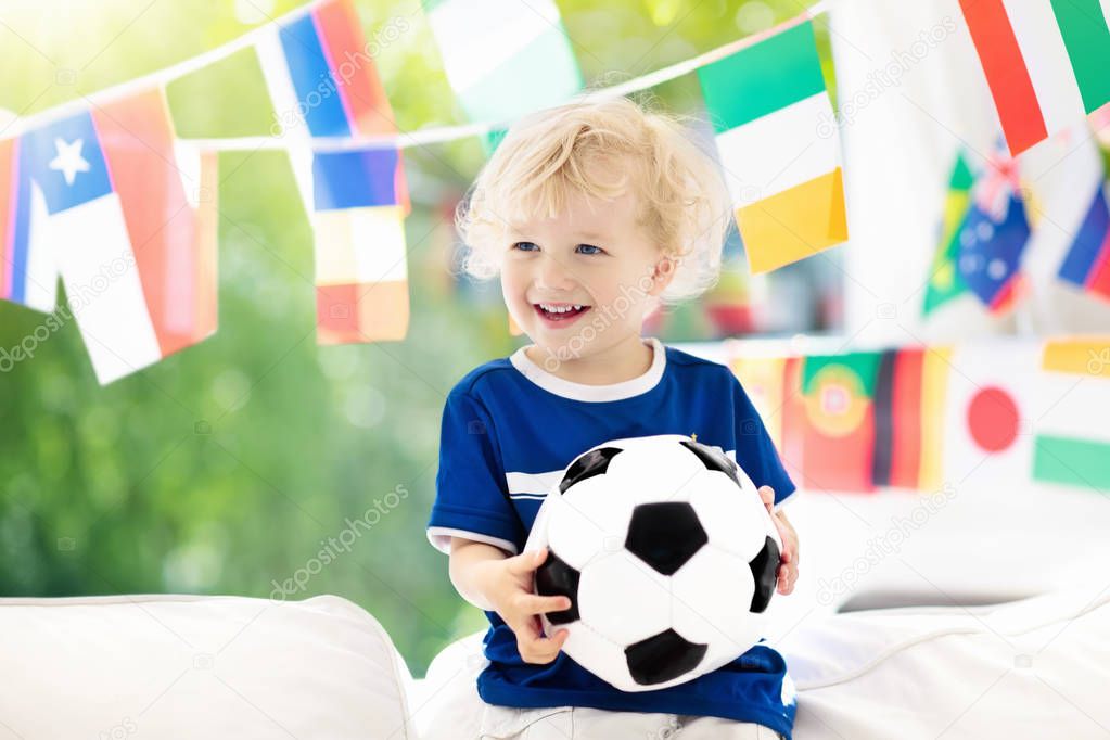 Child watching football game on tv. Little boy in France tricot watching soccer game during championship. Kid fan cheering and supporting national team. Young football player with ball before match.