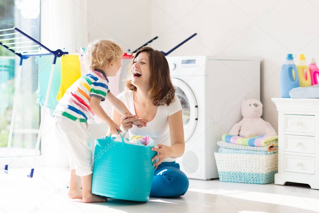 Mother and kids in laundry room with washing machine or tumble dryer. Family chores. Modern household devices and washing detergent in white sunny home. Clean washed clothes on drying rack. 