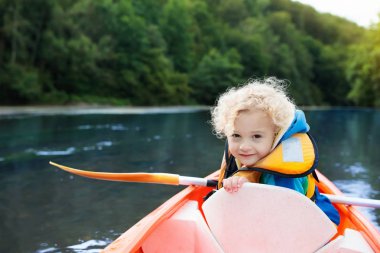 Kano üzerinde kürek çeken çocuk. Çocuklar için yaz kampı. Ailemle kano ve kano gezisi. Kanodaki çocuklar. Küçük çocuk kanoya biniyor. Yaz tatilinde vahşi doğa ve su eğlencesi. Kamp ve balıkçılık.