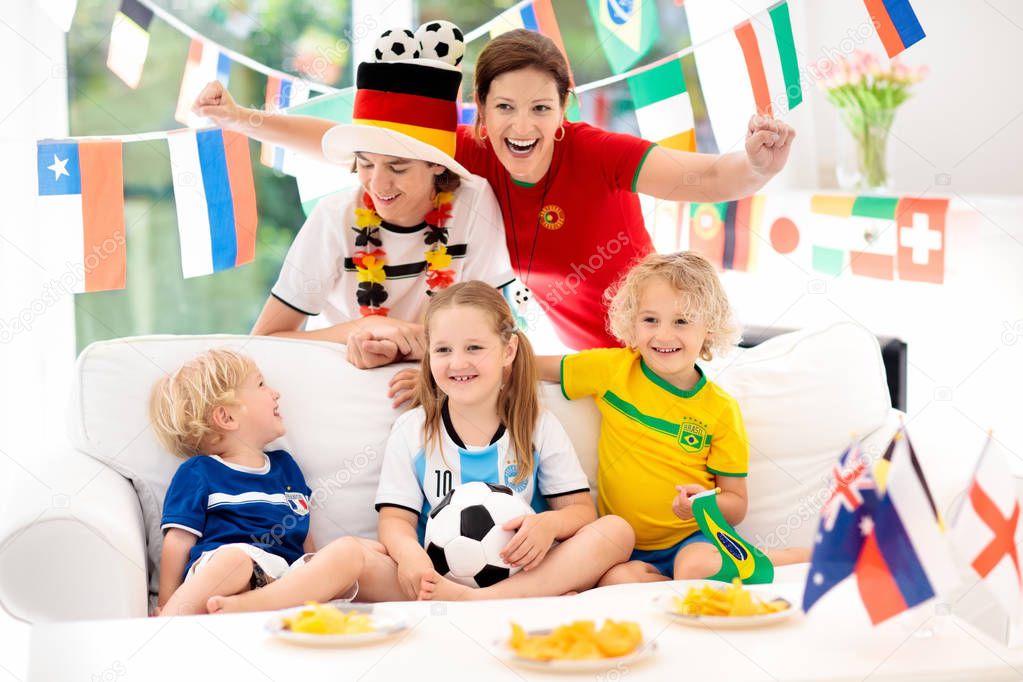 Family with children watching football game on television. Group of young adults and kids in national tricot watch soccer match on tv. Fans cheering and supporting country team at championship.
