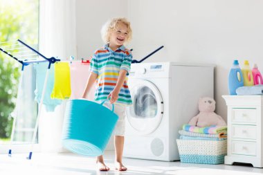 Çocuk Çamaşırhane, çamaşır makinesi ile Oda veya kurutma. Çocuk ile aile işleri yardımcı. Modern ev aygıtları ve çamaşır deterjan beyaz güneşli evinde. Raf kurutma üzerinde temiz yıkanmış kıyafetler. 