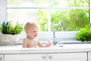 Bebek alarak banyo mutfak lavaboda. Köpük ve sabun köpüğü ile pencere güneşli banyoda ile oynayan çocuk. Küçük çocuk banyo. Su eğlenceli çocuklar için. Hijyen ve Cilt Bakımı Çocuk için. Banyo odası iç