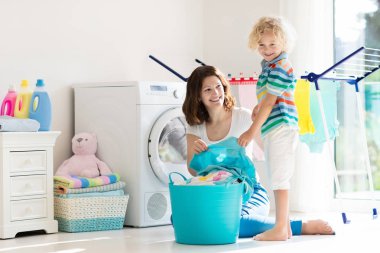 Anne ve çocuklar Çamaşırhane, çamaşır makinesi ile Oda veya kurutma. Aile işleri. Modern ev aygıtları ve çamaşır deterjan beyaz güneşli evinde. Raf kurutma üzerinde temiz yıkanmış kıyafetler. 
