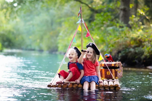 孩子们穿着海盗服装和帽子藏宝箱 与剑在炎热的夏天在河里航行的木排上玩 海盗角色游戏给孩子 家庭的水乐趣 — 图库照片