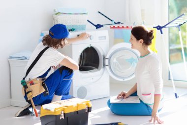 Çamaşır makinesi tamir servisi. İncelenmesi ve onarma Genç teknisyen çamaşır kurutma makinesi. Kırık ev aleti arayan kadın. Müşteri ile tesisatçı. Adam sabitleme çamaşır makinesi.