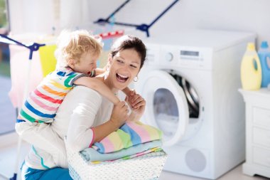 Anne ve çocuklar Çamaşırhane, çamaşır makinesi ile Oda veya kurutma. Aile işleri. Modern ev aygıtları ve çamaşır deterjan beyaz güneşli evinde. Raf kurutma üzerinde temiz yıkanmış kıyafetler. 