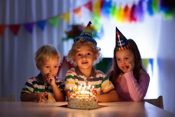 子供の誕生日パーティー 子どもは 暗い部屋でケーキのろうそくを吹き消します 虹の装飾 子供たちのイベント バナー 旗のテーブル セット 女の子と男の子の誕生日プレゼントに 家族のお祝い — ストック写真