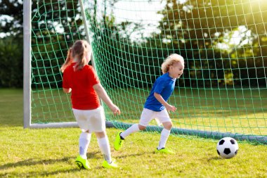 Çocuklar dışarıda futbol oynarlar. Çocuklar futbol maçında gol attılar. Kız ve erkek topa vuruyor. Formalı ve kramponlu koşan çocuk. Okul futbol kulübü. Genç oyuncu için spor eğitimi.