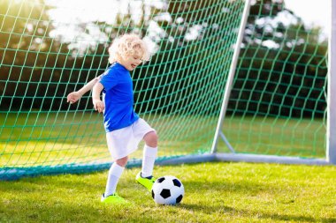 Çocuklar dışarıda futbol oynarlar. Çocuklar futbol maçında gol atıyor. Küçük çocuk topa vuruyor. Formalı ve kramponlu koşan çocuk. Okul futbol kulübü. Genç oyuncu için spor eğitimi.