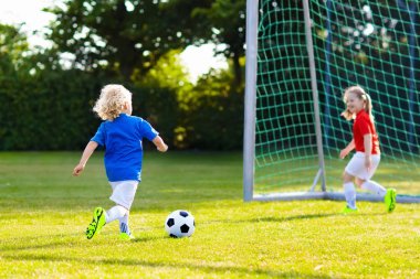 Çocuklar dışarıda futbol oynarlar. Çocuklar futbol maçında gol attılar. Kız ve erkek topa vuruyor. Formalı ve kramponlu koşan çocuk. Okul futbol kulübü. Genç oyuncu için spor eğitimi.