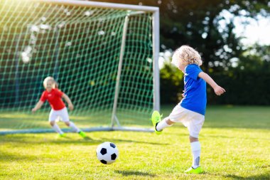 Çocuklar dışarıda futbol oynarlar. Çocuklar futbol maçında gol atıyor. Küçük çocuk topa vuruyor. Formalı ve kramponlu koşan çocuk. Okul futbol kulübü. Genç oyuncu için spor eğitimi.