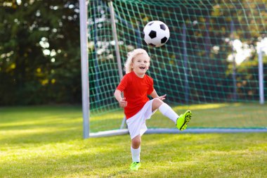 Çocuklar dışarıda futbol oynarlar. Çocuklar futbol maçında gol atıyor. Küçük çocuk topa vuruyor. Formalı ve kramponlu koşan çocuk. Okul futbol kulübü. Genç oyuncu için spor eğitimi.