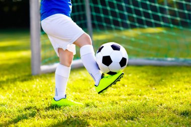 Çocuklar dışarıda futbol oynarlar. Çocuklar futbol maçında gol atıyor. Küçük çocuk topa vuruyor. Formalı ve kramponlu koşan çocuk. Okul futbol kulübü. Genç oyuncu için spor eğitimi.
