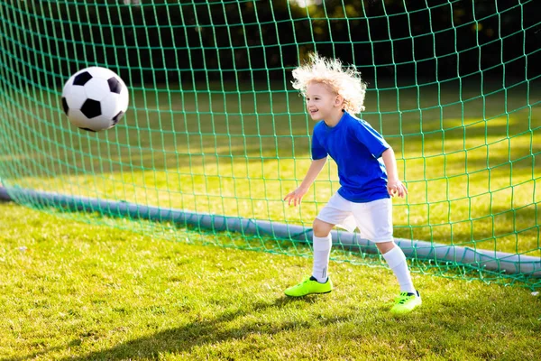 Çocuklar dışarıda futbol oynarlar. Çocuklar futbol maçında gol atıyor. Küçük çocuk topa vuruyor. Formalı ve kramponlu koşan çocuk. Okul futbol kulübü. Genç oyuncu için spor eğitimi.