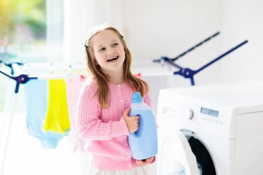 Çocuk Çamaşırhane, çamaşır makinesi ile Oda veya kurutma. Çocuk ile aile işleri yardımcı. Modern ev aygıtları ve çamaşır deterjan beyaz güneşli evinde. Raf kurutma üzerinde temiz yıkanmış kıyafetler. 