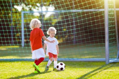 Çocuklar dışarıda futbol oynarlar. Çocuklar futbol maçında gol attılar. Küçük çocuk topa vuruyor. Formalı ve kramponlu koşan çocuk. Okul futbol kulübü. Genç oyuncu için spor eğitimi.