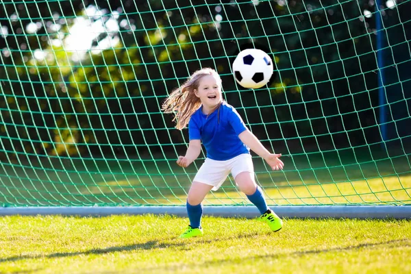 Kids play football on outdoor field. Children score a goal at soccer game. Little girl kicking ball. Running child in team jersey and cleats. School football club. Sports training for young player.