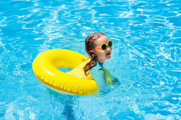 Child with sunglasses in swimming pool. Little girl on inflatable ring. Kid with colorful float. Kids learn to swim and dive in outdoor pool of tropical resort. Sun protection and eye wear. Water fun.