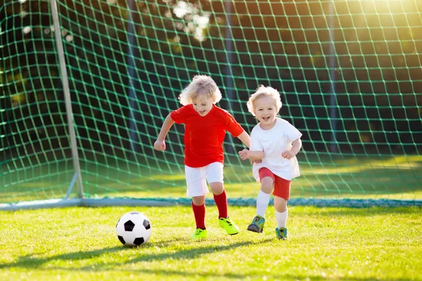 Kids play football on outdoor field. Children score a goal at soccer game. Little boy kicking ball. Running child in team jersey and cleats. School football club. Sports training for young player.