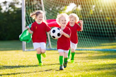 Çocuklar dışarıda futbol oynarlar. Portekiz milli bayrağı taşıyan takım taraftarları. Çocuklar futbol maçında gol attılar. Portekiz formalı ve kramponlu çocuk topa vuruyor. Taraftarlar sahada zaferi kutluyor.