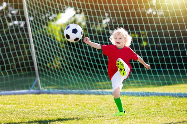 Kids play football on outdoor field. Portugal team fans. Children score a goal at soccer game. Boy in Portuguese jersey and cleats kicking ball. Football club pitch. Sports training for young player.