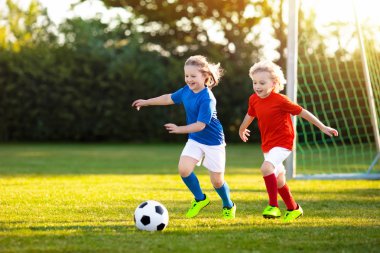Çocuklar dışarıda futbol oynarlar. Çocuklar futbol maçında gol attılar. Kız ve erkek topa vuruyor. Formalı ve kramponlu koşan çocuk. Okul futbol kulübü. Genç oyuncu için spor eğitimi.