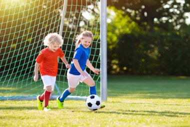Çocuklar dışarıda futbol oynarlar. Çocuklar futbol maçında gol attılar. Kız ve erkek topa vuruyor. Formalı ve kramponlu koşan çocuk. Okul futbol kulübü. Genç oyuncu için spor eğitimi.