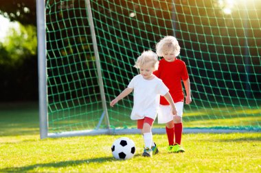 Çocuklar dışarıda futbol oynarlar. Çocuklar futbol maçında gol attılar. Küçük çocuk topa vuruyor. Formalı ve kramponlu koşan çocuk. Okul futbol kulübü. Genç oyuncu için spor eğitimi.