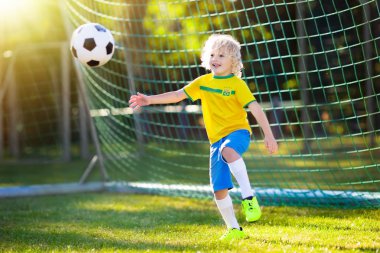 Çocuklar açık sahada futbol oynar. Brezilya takım taraftarları. Çocuk futbol maçında bir gol. Brezilya forması ve ayakkabısı topu tekmeleme içindeki küçük çocuk. Futbol sahası. Spor oyuncu için eğitim.