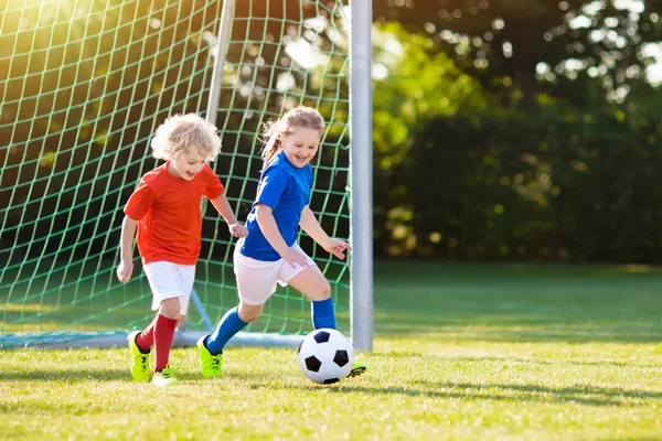 Çocuklar dışarıda futbol oynarlar. Çocuklar futbol maçında gol attılar. Kız ve erkek topa vuruyor. Formalı ve kramponlu koşan çocuk. Okul futbol kulübü. Genç oyuncu için spor eğitimi.