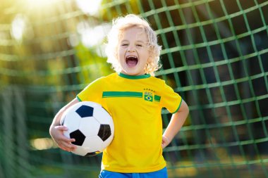 Çocuklar açık sahada futbol oynar. Brezilya takım taraftarları. Çocuk futbol maçında bir gol. Brezilya forması ve ayakkabısı topu tekmeleme içindeki küçük çocuk. Futbol sahası. Spor oyuncu için eğitim.