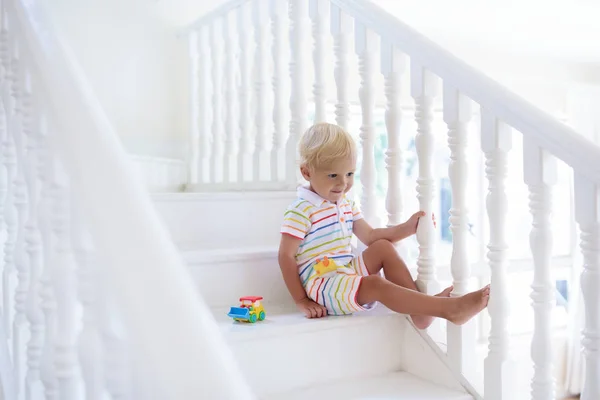 Kid walking stairs in white house. Baby boy playing in sunny staircase. Family moving into new home. Child crawling steps of modern stairway. Foyer and living room interior. Home safety for toddler.