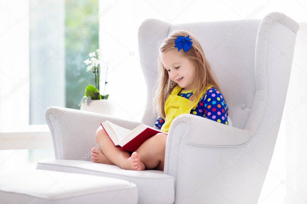 Child reading book. Kids read books. Little girl doing school homework. Preschool kid learning and studying at home. Preschooler in white armchair in white sunny bedroom at home. Children education.