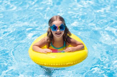 Çocuk yüzme havuzunda şişme yüzüklü. Tropikal tatil sarı kayan nokta üzerinde rahatlatıcı renkli gözlüklü küçük kız. Plaj ve yüzme giymek. Çocuklar için göz güneş koruması. Yüzmeyi çocuk öğrenmek.