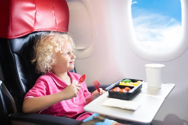 Child in airplane window seat. Kids flight meal. Children fly. Special inflight menu, food and drink for baby and kid. Little boy eating healthy lunch in airplane. Travel with kids. Family vacation.