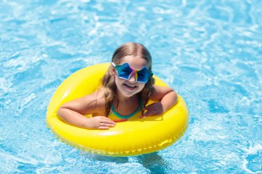 Çocuk yüzme havuzunda şişme yüzüklü. Tropikal tatil sarı kayan nokta üzerinde rahatlatıcı renkli gözlüklü küçük kız. Plaj ve yüzme giymek. Çocuklar için göz güneş koruması. Yüzmeyi çocuk öğrenmek.